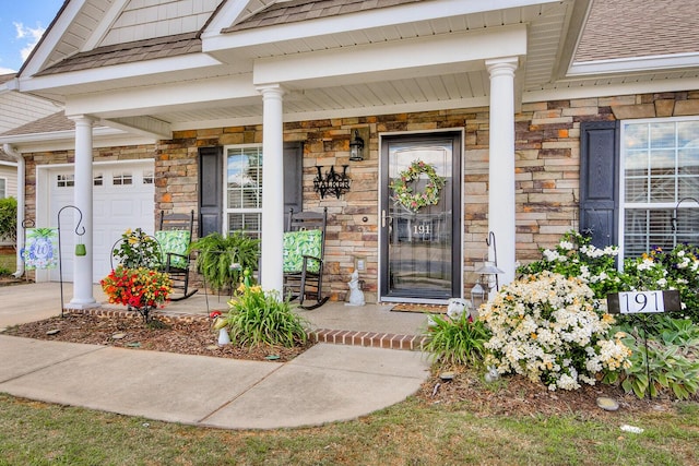 view of exterior entry with covered porch, stone siding, roof with shingles, and a garage