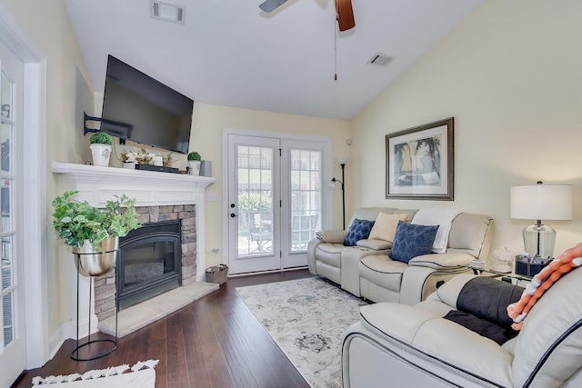 living room featuring vaulted ceiling, wood finished floors, ceiling fan, and a stone fireplace