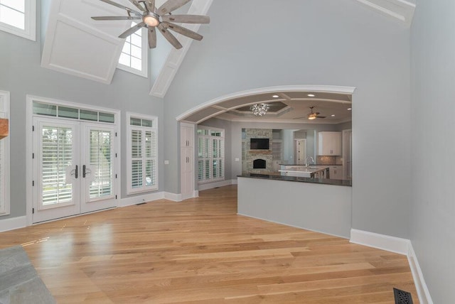 unfurnished living room featuring french doors, light hardwood / wood-style flooring, ceiling fan, and a high ceiling