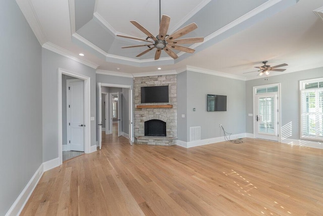 unfurnished living room featuring a raised ceiling, crown molding, light hardwood / wood-style flooring, ceiling fan, and a fireplace