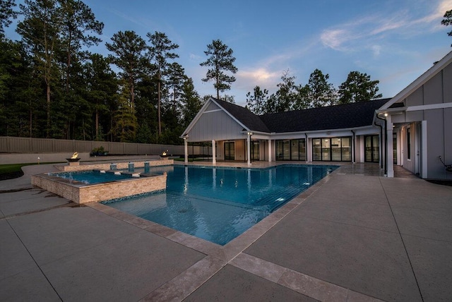 pool at dusk featuring an in ground hot tub and a patio area