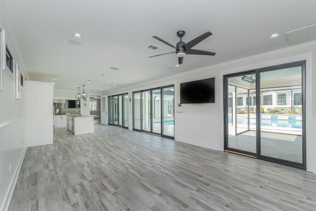 unfurnished living room featuring ceiling fan, crown molding, a wealth of natural light, and light hardwood / wood-style flooring