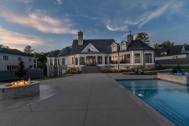 back house at dusk with a fenced in pool, a sunroom, a patio, and a fire pit