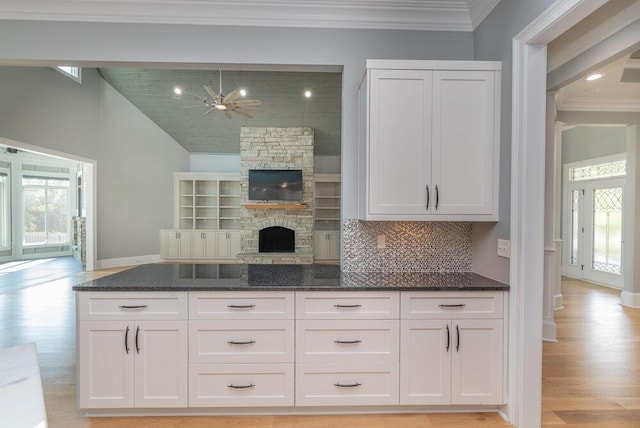 kitchen with backsplash, ceiling fan, dark stone countertops, a fireplace, and white cabinetry