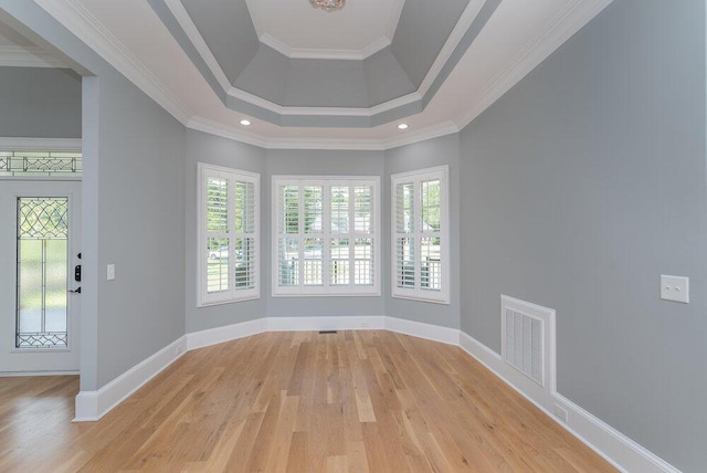 empty room featuring a tray ceiling, crown molding, a towering ceiling, and light wood-type flooring