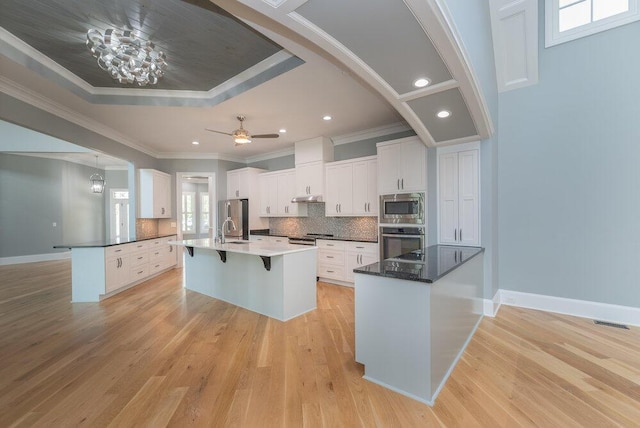 kitchen with light hardwood / wood-style floors, a tray ceiling, white cabinets, a kitchen bar, and appliances with stainless steel finishes