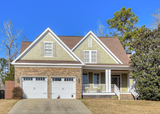 craftsman-style house with a porch, stone siding, driveway, and a front lawn