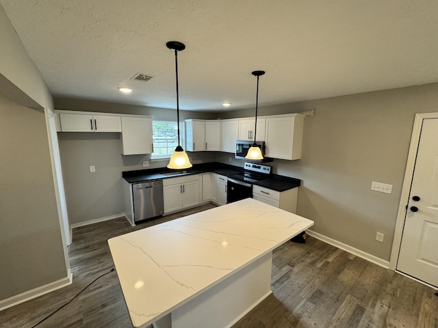 kitchen with white cabinetry, hanging light fixtures, dark hardwood / wood-style floors, dark stone counters, and appliances with stainless steel finishes