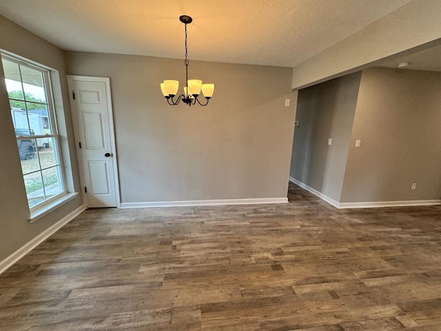 unfurnished room with a notable chandelier, dark hardwood / wood-style floors, and a textured ceiling