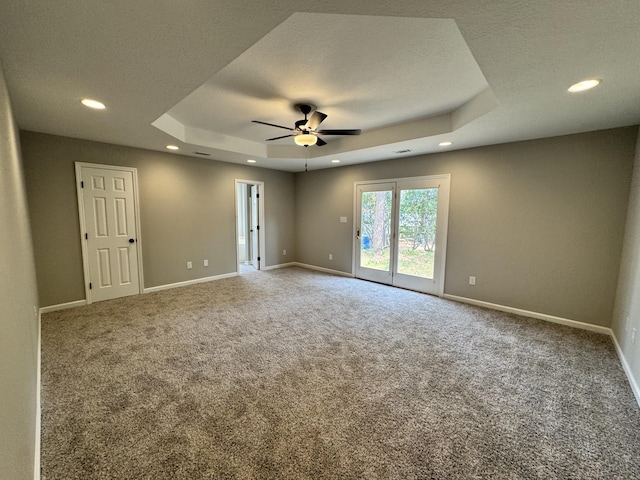 carpeted empty room featuring a raised ceiling, ceiling fan, and a textured ceiling