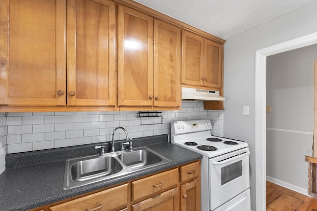 kitchen with brown cabinets, white range with electric cooktop, dark countertops, decorative backsplash, and under cabinet range hood