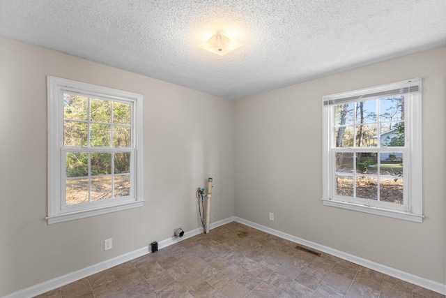 spare room featuring visible vents, plenty of natural light, a textured ceiling, and baseboards