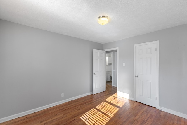 unfurnished bedroom featuring a textured ceiling, wood finished floors, and baseboards