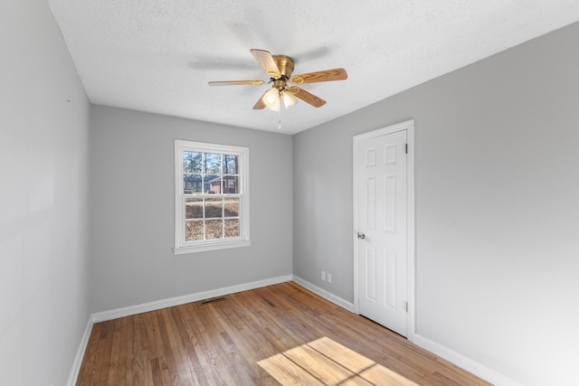 empty room featuring ceiling fan, a textured ceiling, baseboards, and wood finished floors