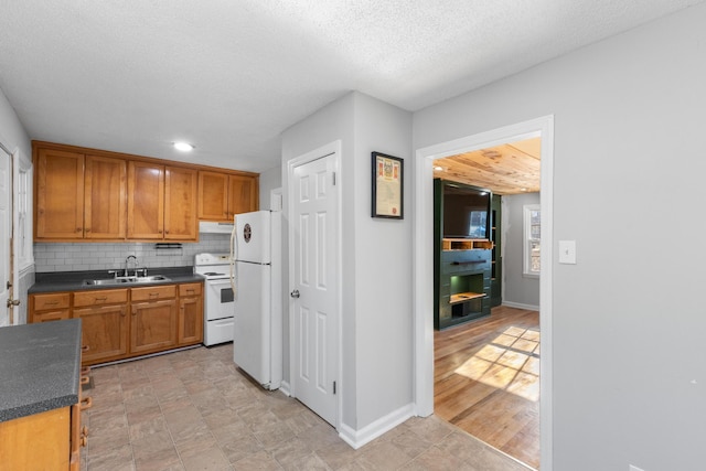 kitchen with dark countertops, backsplash, a sink, white appliances, and under cabinet range hood