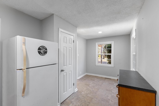 kitchen with freestanding refrigerator, dark countertops, a textured ceiling, and baseboards