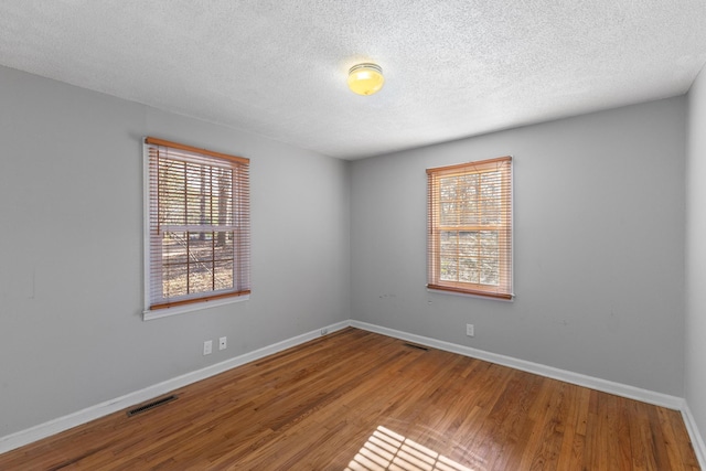 unfurnished room with wood finished floors, visible vents, and baseboards