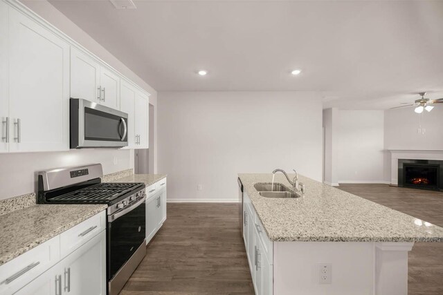 kitchen featuring a center island with sink, a lit fireplace, a sink, appliances with stainless steel finishes, and white cabinetry