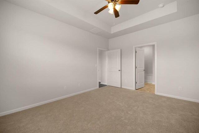 unfurnished bedroom featuring light carpet, a raised ceiling, connected bathroom, baseboards, and ceiling fan