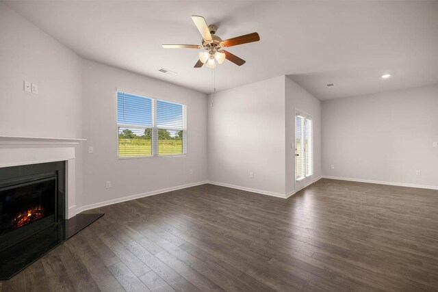 unfurnished living room featuring a wealth of natural light, a glass covered fireplace, visible vents, and dark wood-style flooring