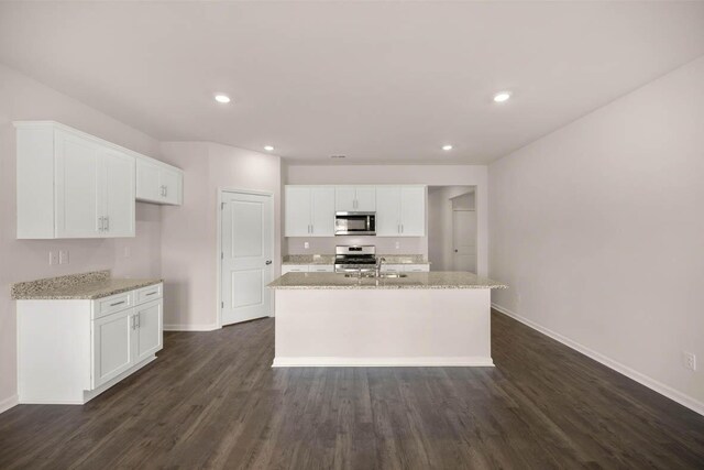 kitchen with dark wood-type flooring, a sink, stainless steel appliances, white cabinets, and light stone countertops