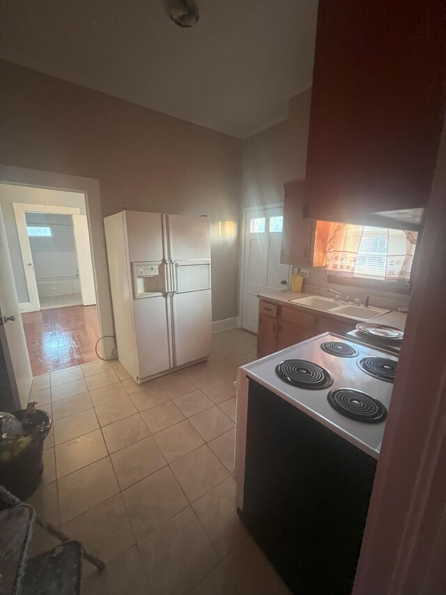 kitchen with electric range, white fridge with ice dispenser, sink, and light tile patterned floors