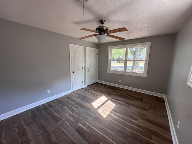 unfurnished bedroom featuring ceiling fan, dark hardwood / wood-style floors, a textured ceiling, and two closets