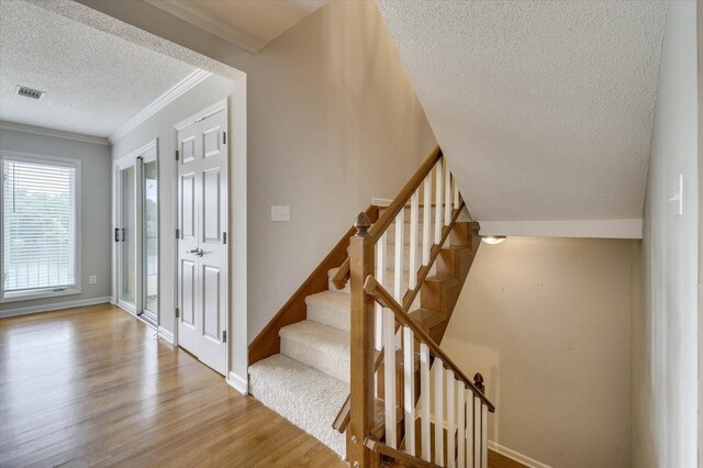 stairs with crown molding, a textured ceiling, and hardwood / wood-style flooring