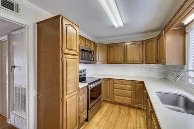 kitchen with backsplash, sink, stainless steel appliances, and ornamental molding