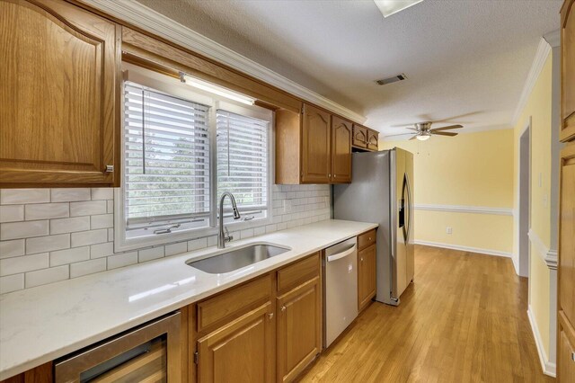 kitchen with sink, a textured ceiling, appliances with stainless steel finishes, tasteful backsplash, and light hardwood / wood-style floors