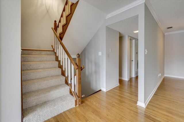 staircase featuring a textured ceiling, hardwood / wood-style flooring, and crown molding