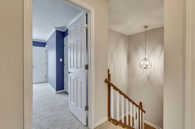 hallway with a textured ceiling, light colored carpet, an inviting chandelier, and ornamental molding