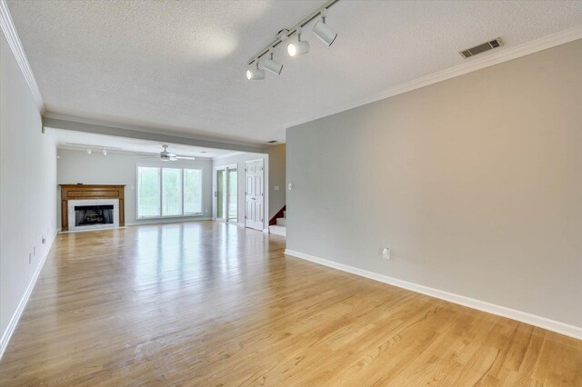 unfurnished living room featuring light hardwood / wood-style floors, ornamental molding, a textured ceiling, and track lighting