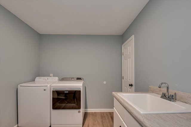 clothes washing area featuring washer and clothes dryer, cabinets, sink, and light hardwood / wood-style flooring