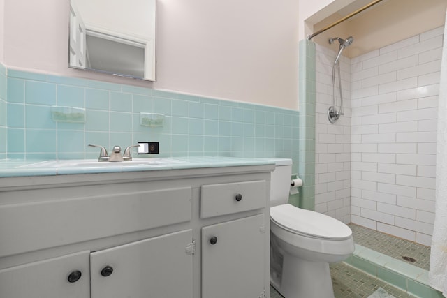 bathroom with tiled shower, vanity, toilet, and tile walls