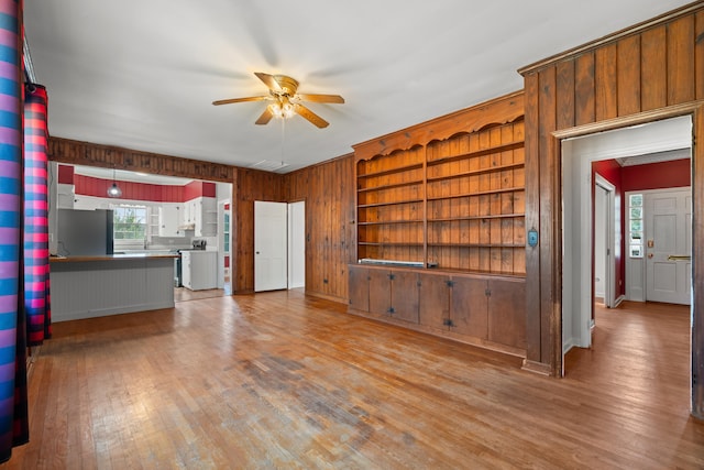 unfurnished living room with wooden walls, light hardwood / wood-style floors, and ceiling fan