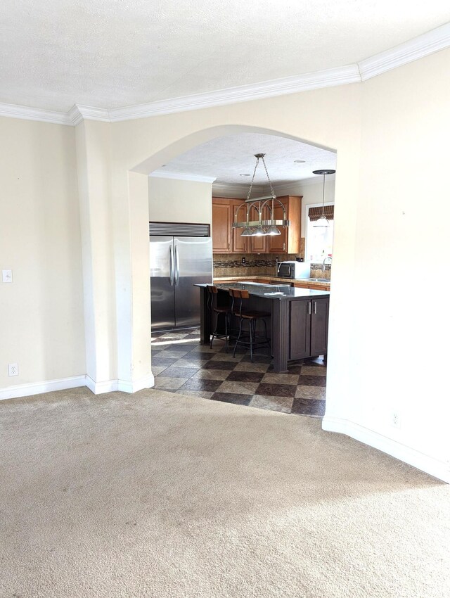 kitchen with a breakfast bar, dark colored carpet, crown molding, and built in refrigerator