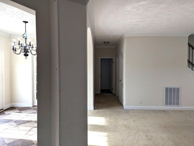 hallway with a textured ceiling, crown molding, carpet floors, visible vents, and an inviting chandelier