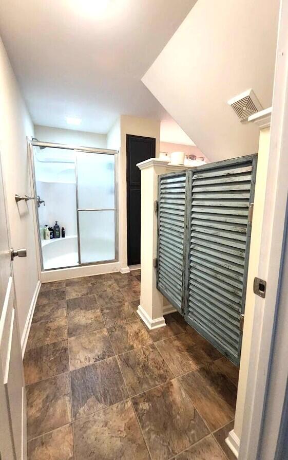 interior space with a shower stall, visible vents, baseboards, and stone finish flooring