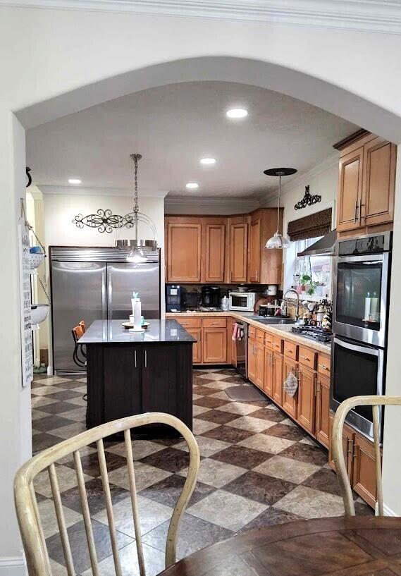 kitchen with arched walkways, appliances with stainless steel finishes, ornamental molding, decorative light fixtures, and recessed lighting