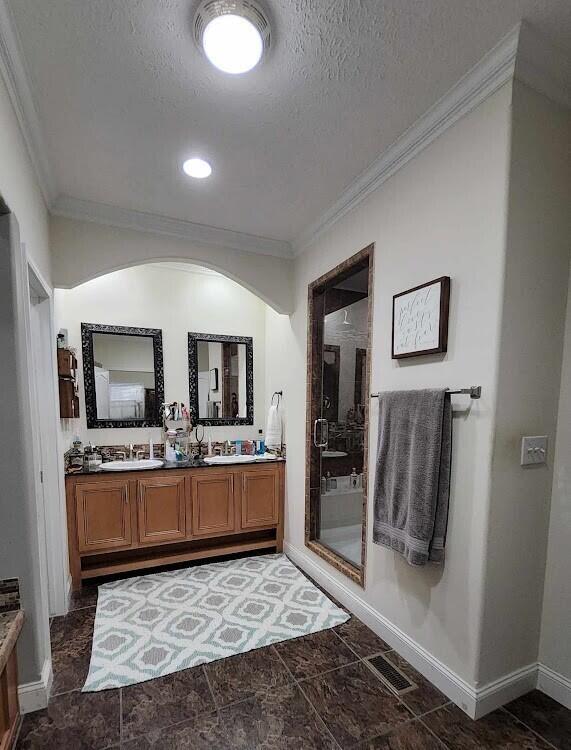 bathroom with double vanity, a stall shower, ornamental molding, and a textured ceiling