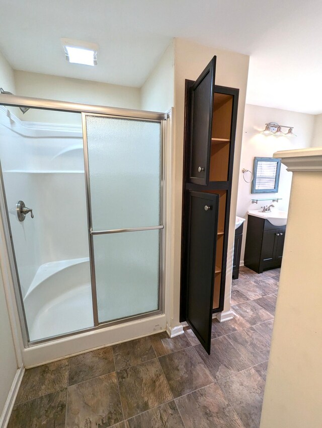 full bathroom featuring a stall shower, stone finish flooring, vanity, and baseboards