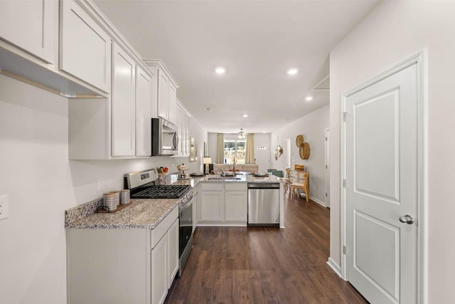 kitchen with light stone countertops, white cabinetry, stainless steel appliances, dark hardwood / wood-style floors, and kitchen peninsula