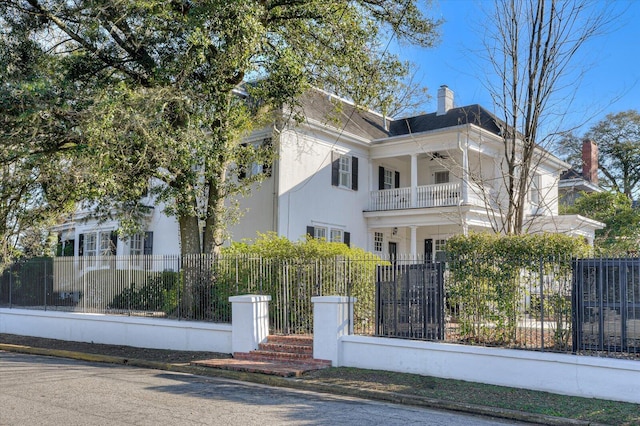 neoclassical home with a fenced front yard, a chimney, a balcony, and stucco siding