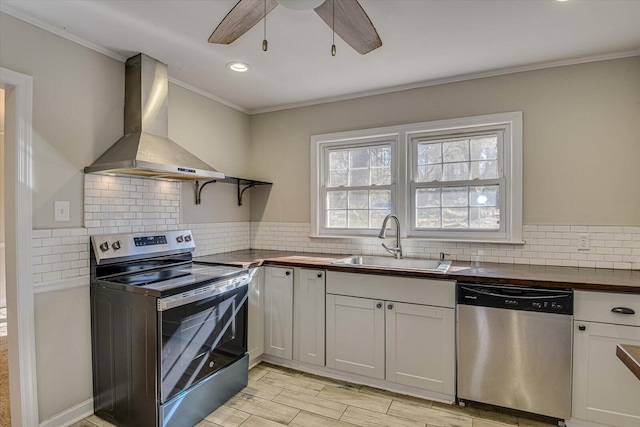 kitchen with appliances with stainless steel finishes, wood counters, sink, white cabinets, and wall chimney range hood