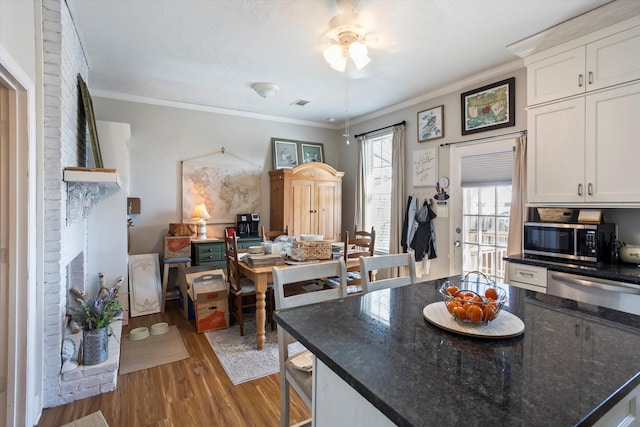 kitchen with stainless steel microwave, wood finished floors, white cabinetry, and crown molding