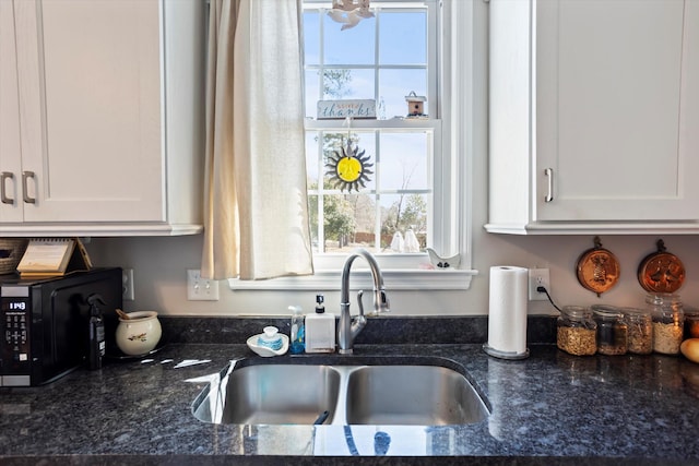 kitchen featuring dark stone counters, black microwave, a sink, and white cabinetry