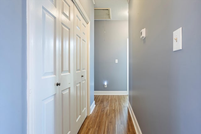 hallway with a textured ceiling, wood finished floors, attic access, and baseboards