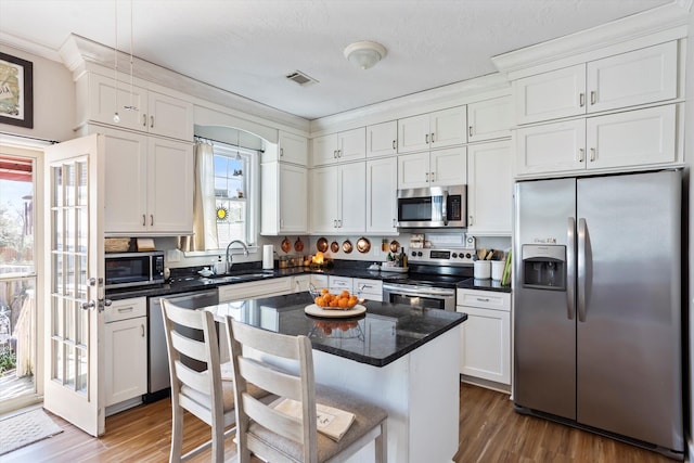 kitchen featuring visible vents, appliances with stainless steel finishes, white cabinets, a sink, and wood finished floors