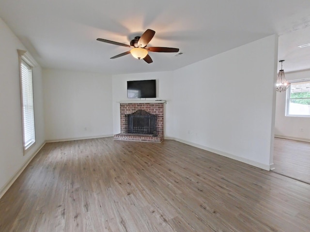 unfurnished living room with baseboards, wood finished floors, ceiling fan with notable chandelier, and a fireplace